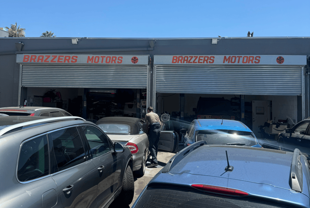 Brazzers Motors auto repair shop exterior in Canoga Park, featuring a mechanic working on a vehicle among parked cars, emphasizing vehicle repair services and customer care.