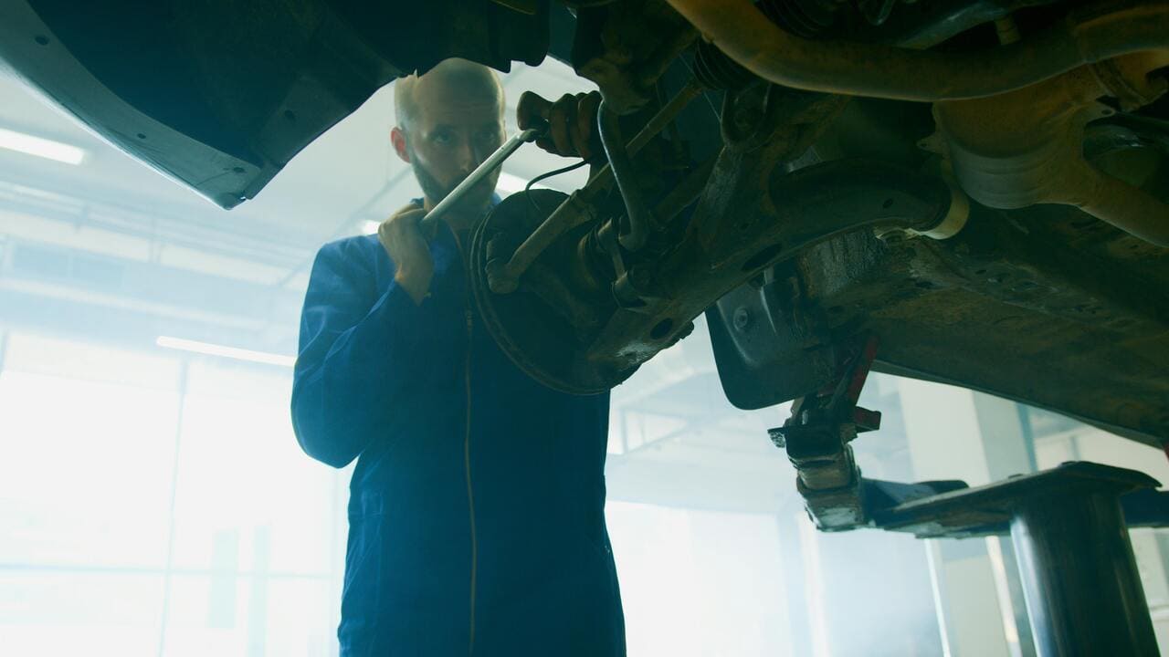 Mechanic working on vehicle suspension in auto repair shop, focusing on vehicle maintenance and repair services in Canoga Park.